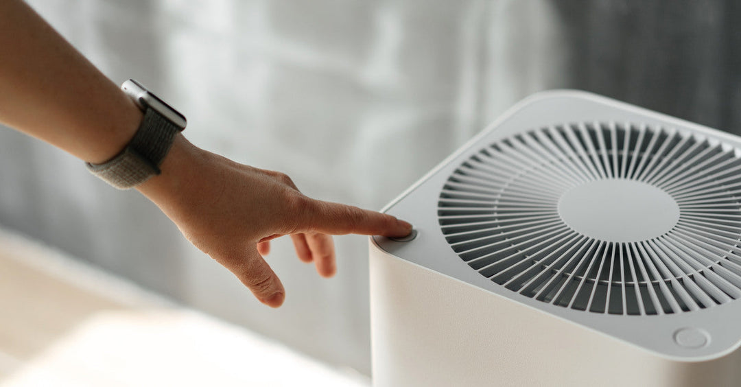 A person wearing a smart watch pressing a button on the top of an air purifier with the number "001" showing on its side.